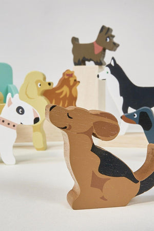 A colorful wooden dog figure, styled with a brown and black design, sits in front of a variety of other wooden dog toys in playful poses, showcasing Tender Leafs Waggy.