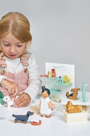 A young girl plays with the Tender Leaf Wooden Toys Waggy Tails Dog Salon set, featuring colorful wooden figures of dogs and a groomer, promoting imaginative play and sustainable materials.