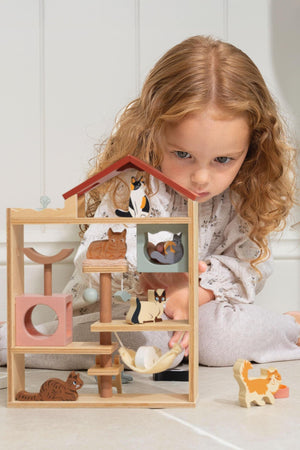 A young girl with curly hair focuses on a wooden cat hotel featuring colorful, handcrafted cats. The charming design encourages imaginative play and storytelling in a cozy setting.