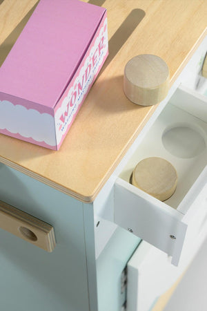 A pastel-colored wooden laundry unit features a smooth light wood countertop and a white drawer, showcasing two round wooden pieces. The design is playful and suitable for childrens imaginative play.