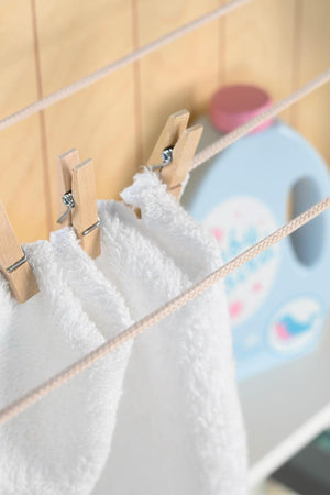 A close-up of white towels hanging on a wooden clothesline, secured with clothespins. In the background, a blue laundry detergent bottle adds a playful touch to the scene.