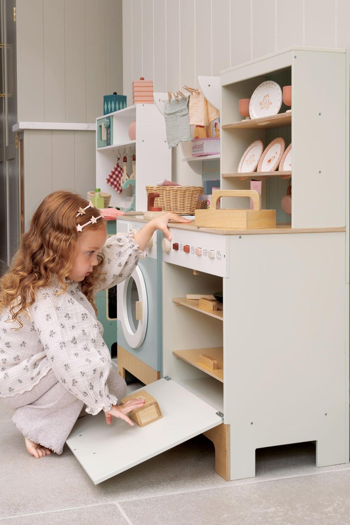 Child playing with wooden dishwasher with shelves and toy utensils