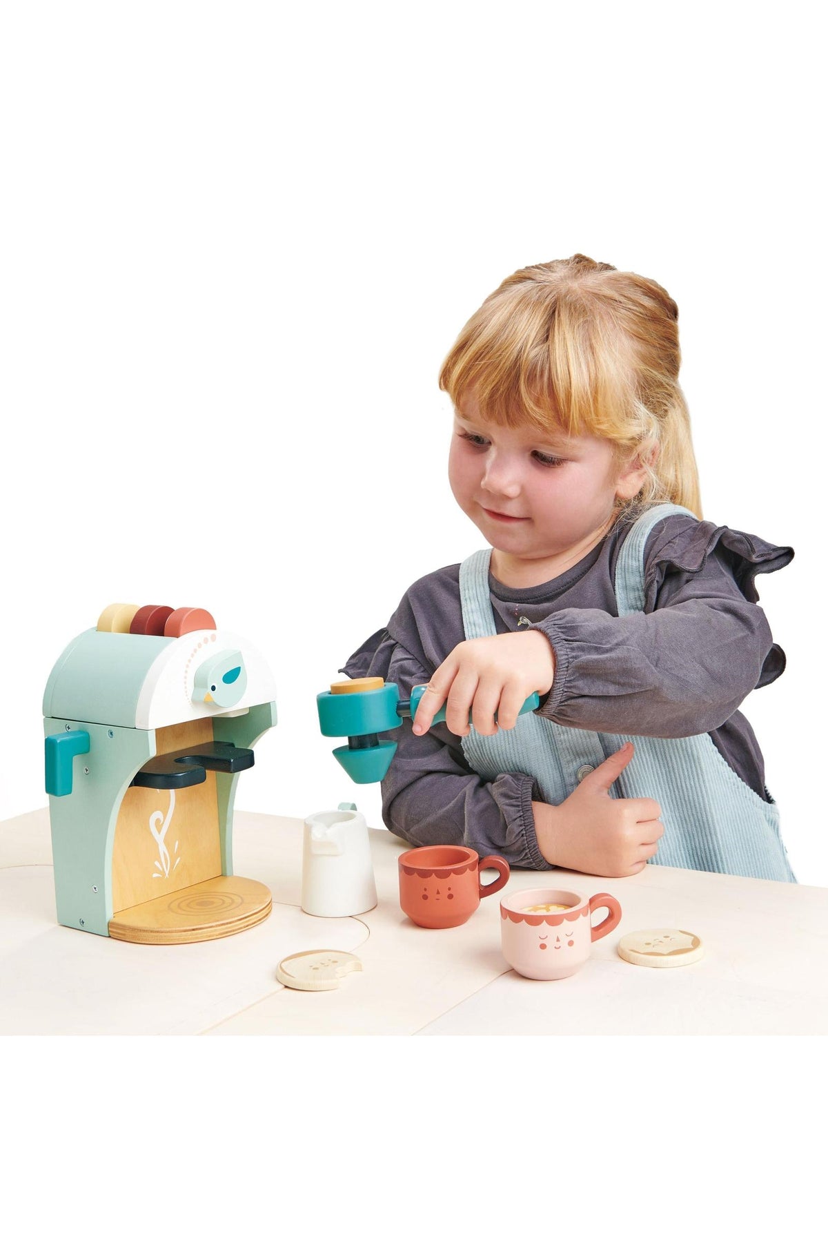 A child plays with a Tender Leaf wooden babyccino maker, featuring pastel colors and charming coffee cups on a light.