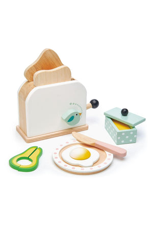 A wooden toaster set featuring a white toaster, two toast slices, a knife, a plate, and avocado slices.