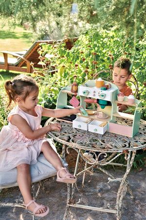 Two children play at a rustic outdoor table with the Tender Leaf Wooden Toys Bird’s Nest Café, featuring colorful accessories.