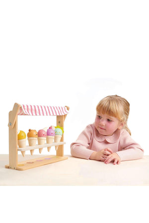 A child interacts with a wooden ice cream shop featuring five colorful cones, each with a friendly face.