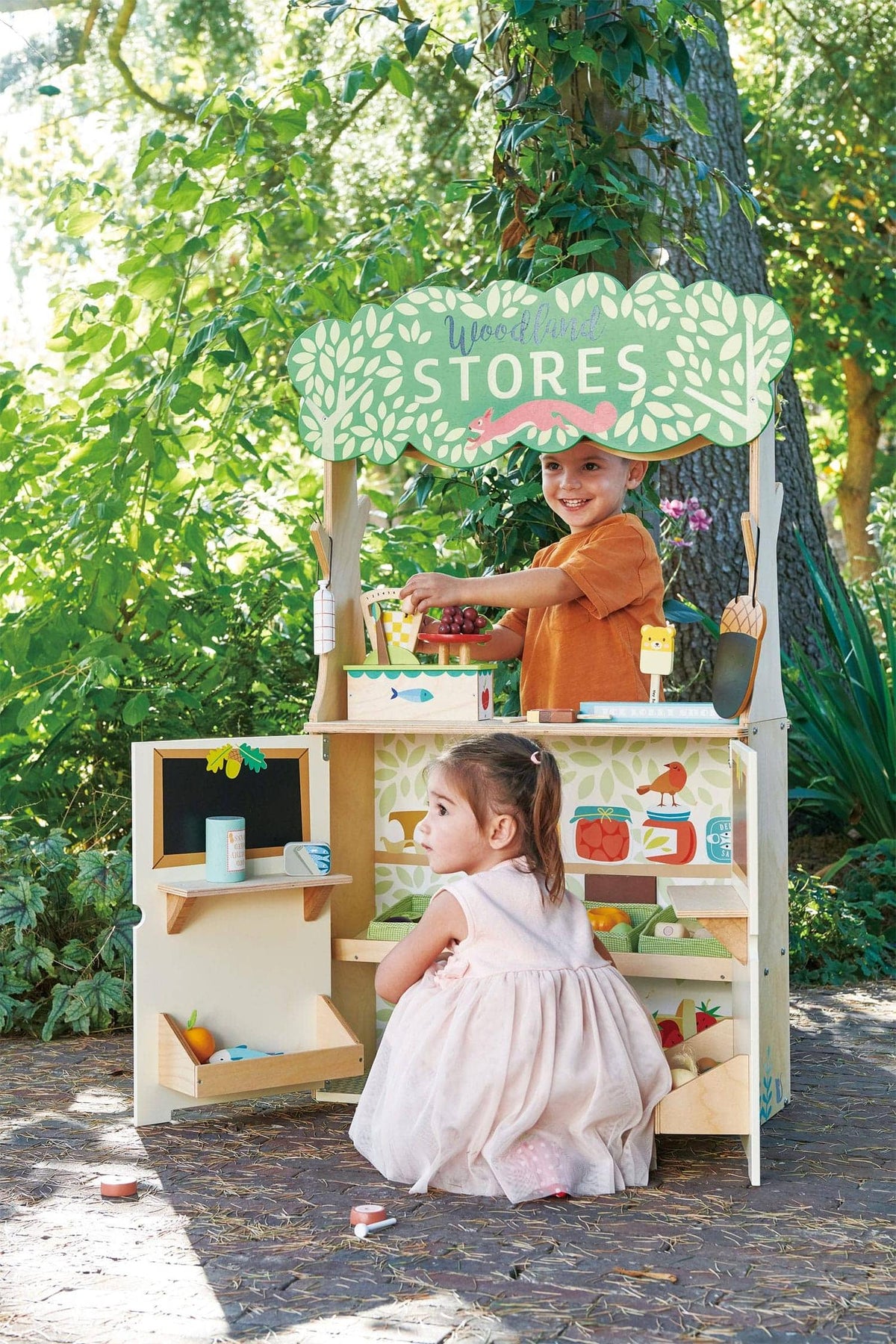 Two children play with a Tender Leaf Wooden Toys Woodland Stores set, featuring colorful designs and eco-friendly materials.