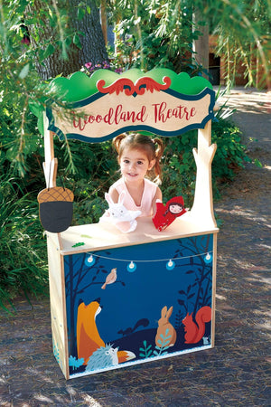 Child playing at a colorful wooden Woodland Theatre playset outdoors, with animal illustrations and puppet toys.