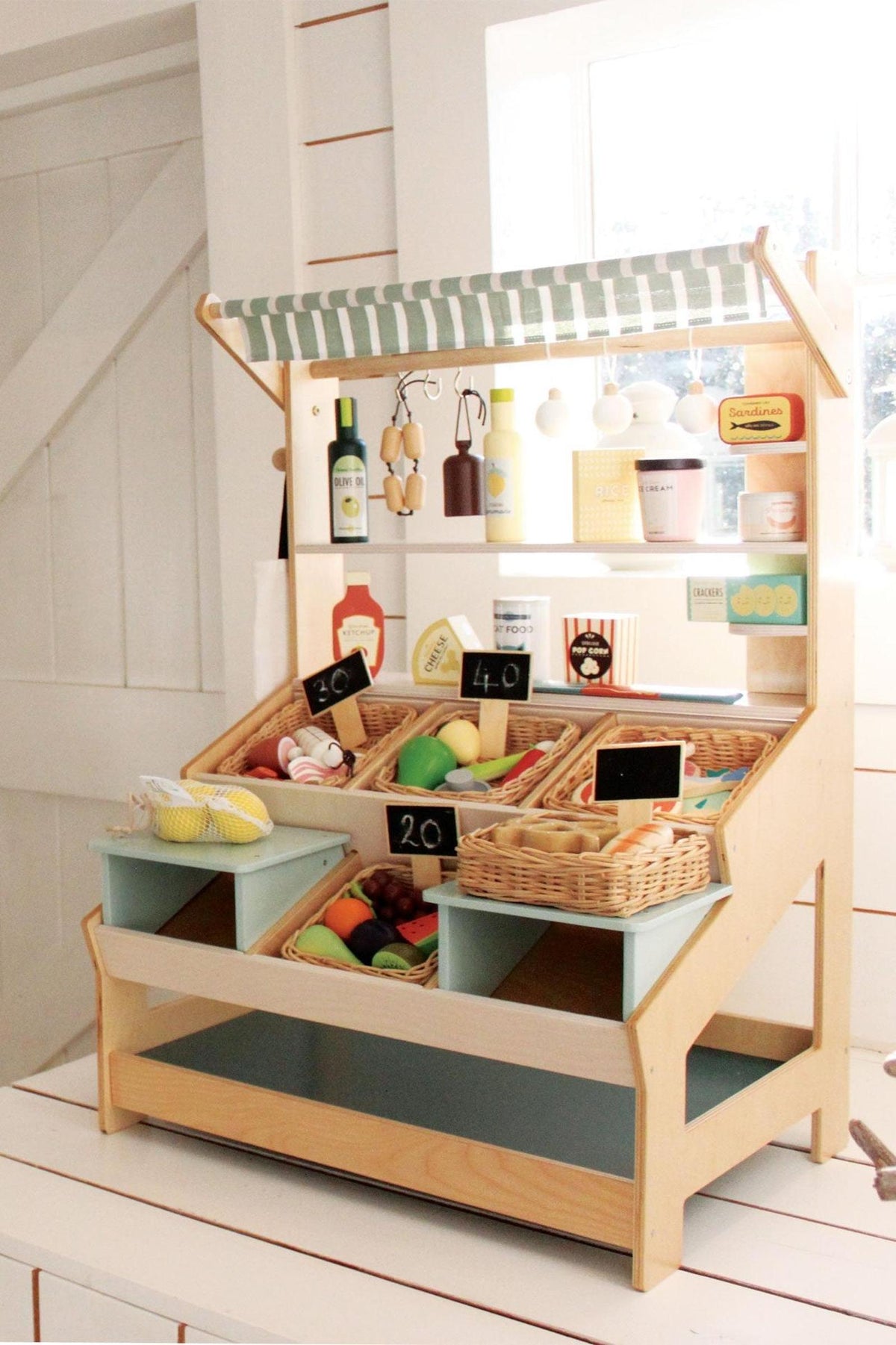 Wooden market stall with a striped canopy, featuring baskets filled with colorful play food and bottles. Perfect for imaginative play.