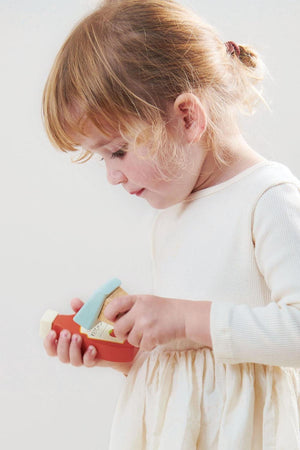 A child in a cream dress plays with a colorful wooden toy scanner, focused and smiling.