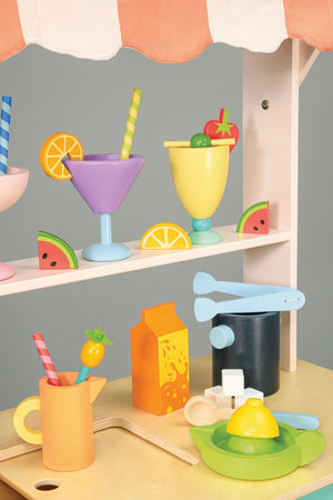 Colorful wooden drink set with cups, fruit slices, and straws under a striped awning on a wooden trolley.
