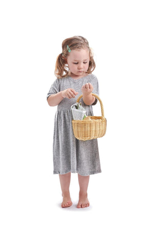 A young girl in a gray dress holds a wicker basket, appearing thoughtful as she examines its contents.