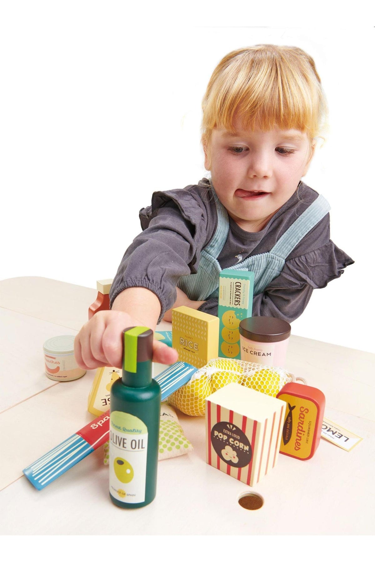 A young child interacts with a colorful wooden grocery set, featuring items like olive oil and popcorn, promoting imaginative play.