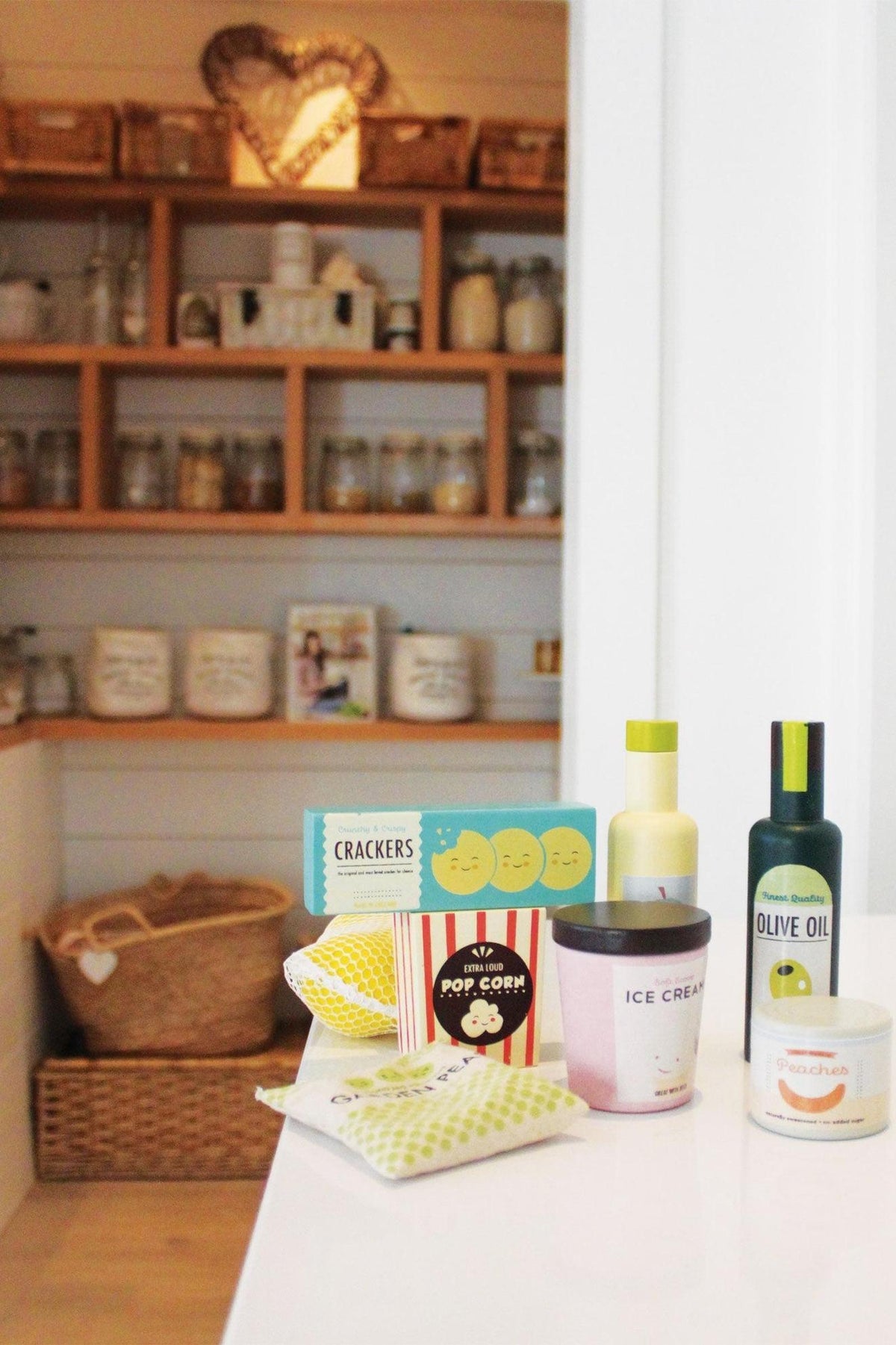 A bright kitchen shelf displays wooden grocery items, including an ice cream tub, olive oil, and popcorn, arranged neatly.