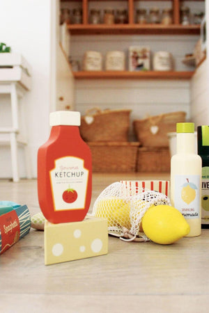 A colorful wooden grocery set featuring a ketchup bottle, lemons, and other food items, set in a bright, inviting space.