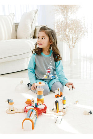 A young girl smiles while playing with a colorful wooden toy set on a light-colored carpet in a bright room.
