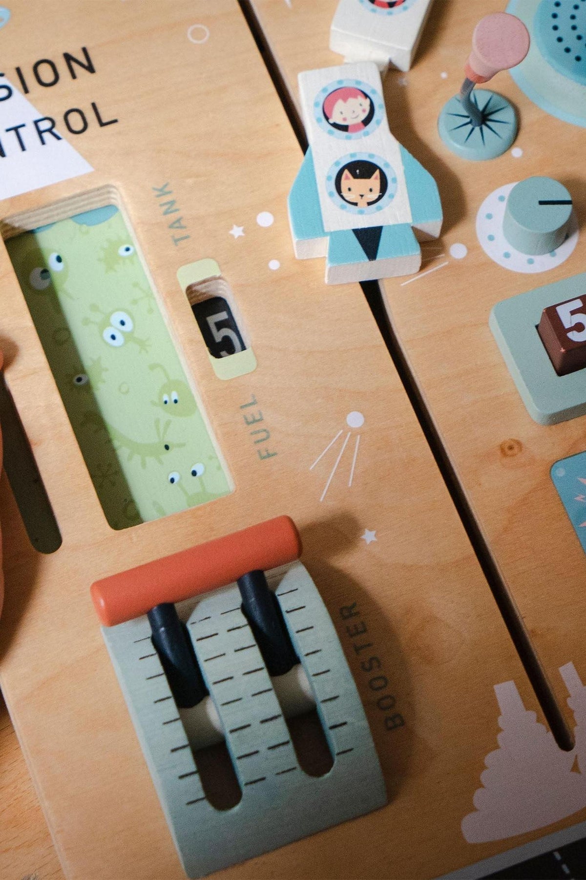 Close-up of a wooden toy space station with colorful interactive elements, featuring a fuel tank and booster controls.