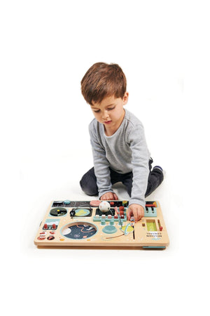 A young boy sits on the floor, exploring a colorful wooden space station playset with various interactive features.