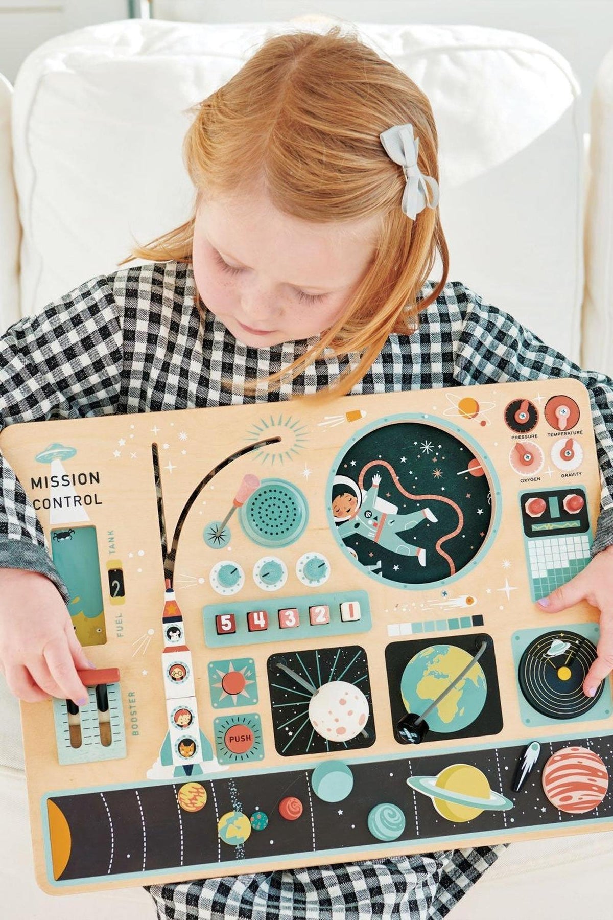 A child holds a colorful wooden space station play board featuring interactive buttons and illustrations, promoting imaginative play.
