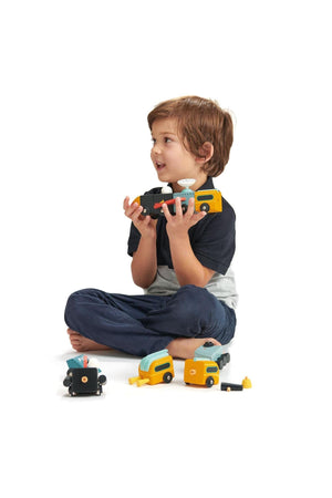 A child sits on the floor, holding a colorful wooden toy vehicle, surrounded by other toy components from the Tender.