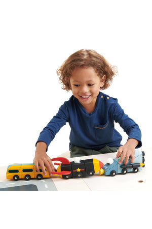 A smiling child plays with colorful wooden toy vehicles, connecting them on a play surface.