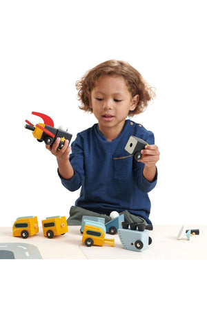 A young child examines colorful wooden toy vehicles, showcasing creativity and imaginative play with sustainable materials.