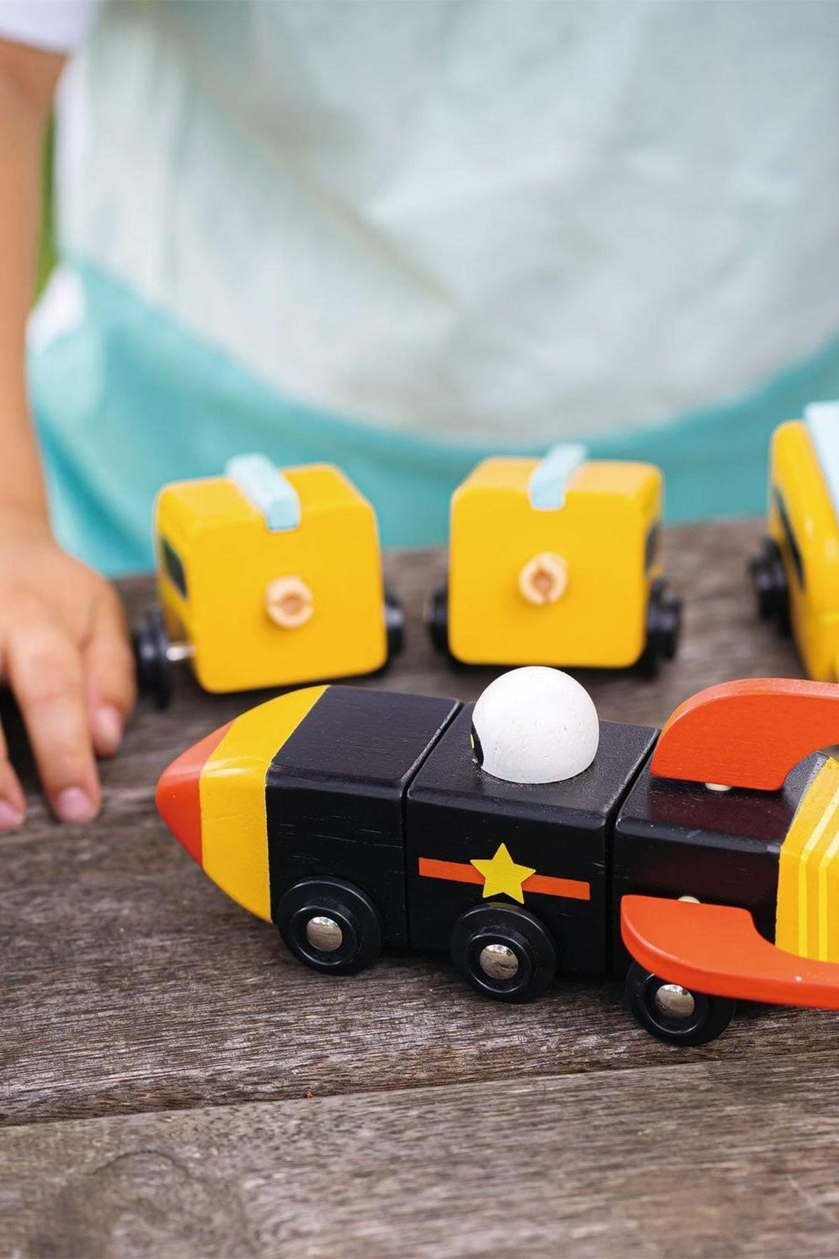 A child assembles colorful wooden toys, including a black and yellow rocket with a white ball, on a wooden table.