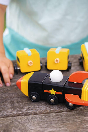 A child assembles colorful wooden toys, including a black and yellow rocket with a white ball, on a wooden table.