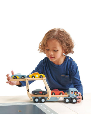 A young child plays with a Tender Leaf wooden car transporter, featuring a detachable carrier and colorful super cars.