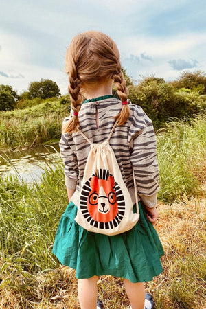 A young girl with braided hair stands by a waterway, wearing a striped shirt and green dress.