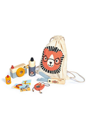 A beige drawstring bag featuring a lion design holds wooden safari adventure toys, including a camera, water bottle, penknife, and mosquito repellent, suitable for children ages 3 and up.