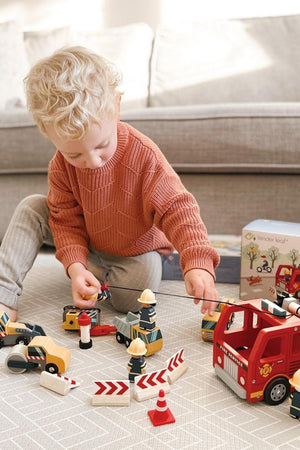 A young child plays with Tender Leaf wooden toys, including a red fire engine, on a light-colored rug.