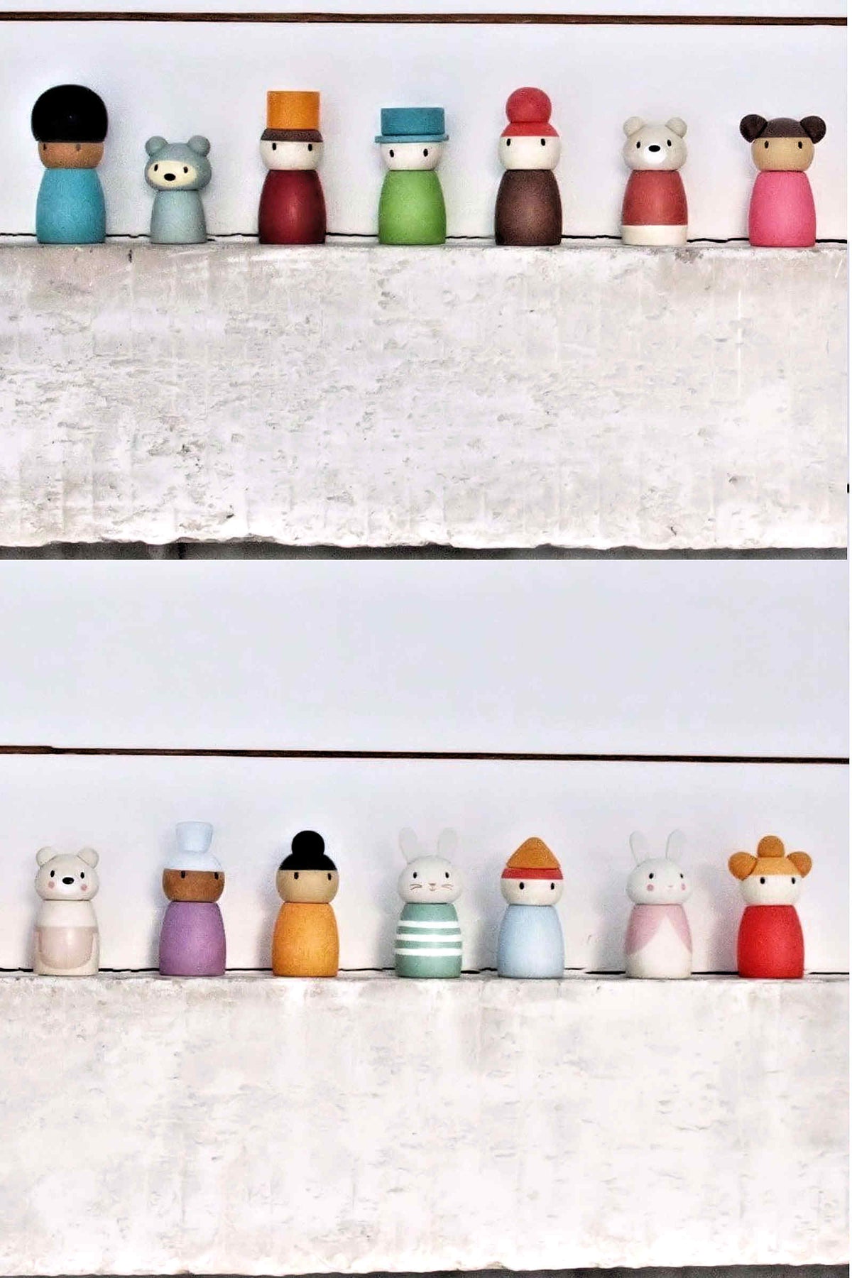 A colorful collection of wooden characters stands on a white shelf, featuring various designs and gentle water-based stains.