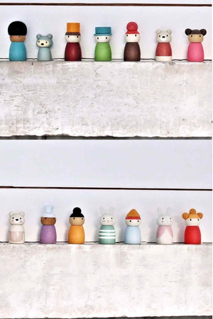 A colorful collection of wooden characters stands on a white shelf, featuring various designs and gentle water-based stains.