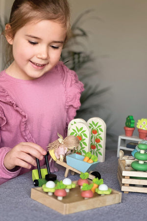 A young girl plays with a wooden garden set, featuring colorful vegetables and a wheelbarrow. The eco-friendly toys encourage imaginative play, showcasing Tender Leafs sustainable design and craftsmanship.