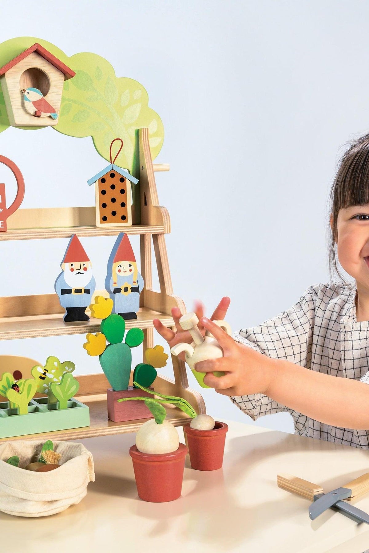 A young child interacts with a colorful wooden garden center, featuring vibrant plants, garden tools, and charming gnome figures. The display is constructed from sustainable materials, promoting eco-friendly play.