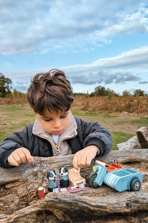 A young boy plays outdoors with a Tender Leaf wooden toy set featuring two animal figures, a picnic basket.
