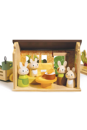 A colorful wooden playset features four bunny figures in a cozy garden shed, surrounded by vegetables and gardening tools.