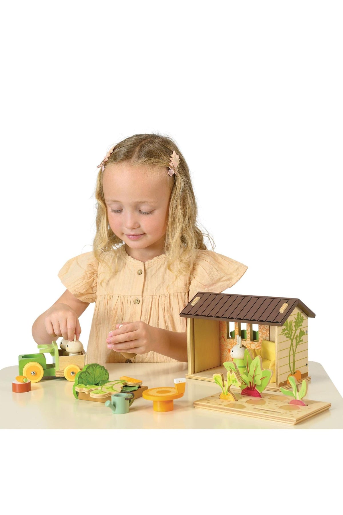 A young girl plays with the Tender Leaf Wooden Toys Bunnys Carrot Patch set, featuring a cozy shed and colorful vegetable pieces, promoting imaginative gardening play and eco-friendly fun.