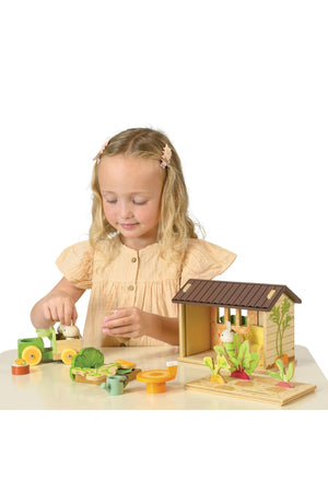 A young girl plays with the Tender Leaf Wooden Toys Bunnys Carrot Patch set, featuring a cozy shed and colorful vegetable pieces, promoting imaginative gardening play and eco-friendly fun.