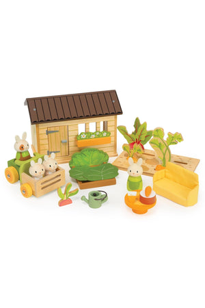 A wooden toy set featuring a cozy shed, three bunny figures, and various vegetable accessories like carrots and a watering can, encouraging imaginative gardening play for young children.