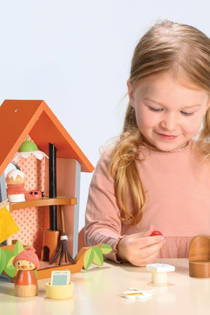 A child plays with a Tender Leaf Wooden Toys birdhouse set, featuring colorful wooden figures and a mini broom.