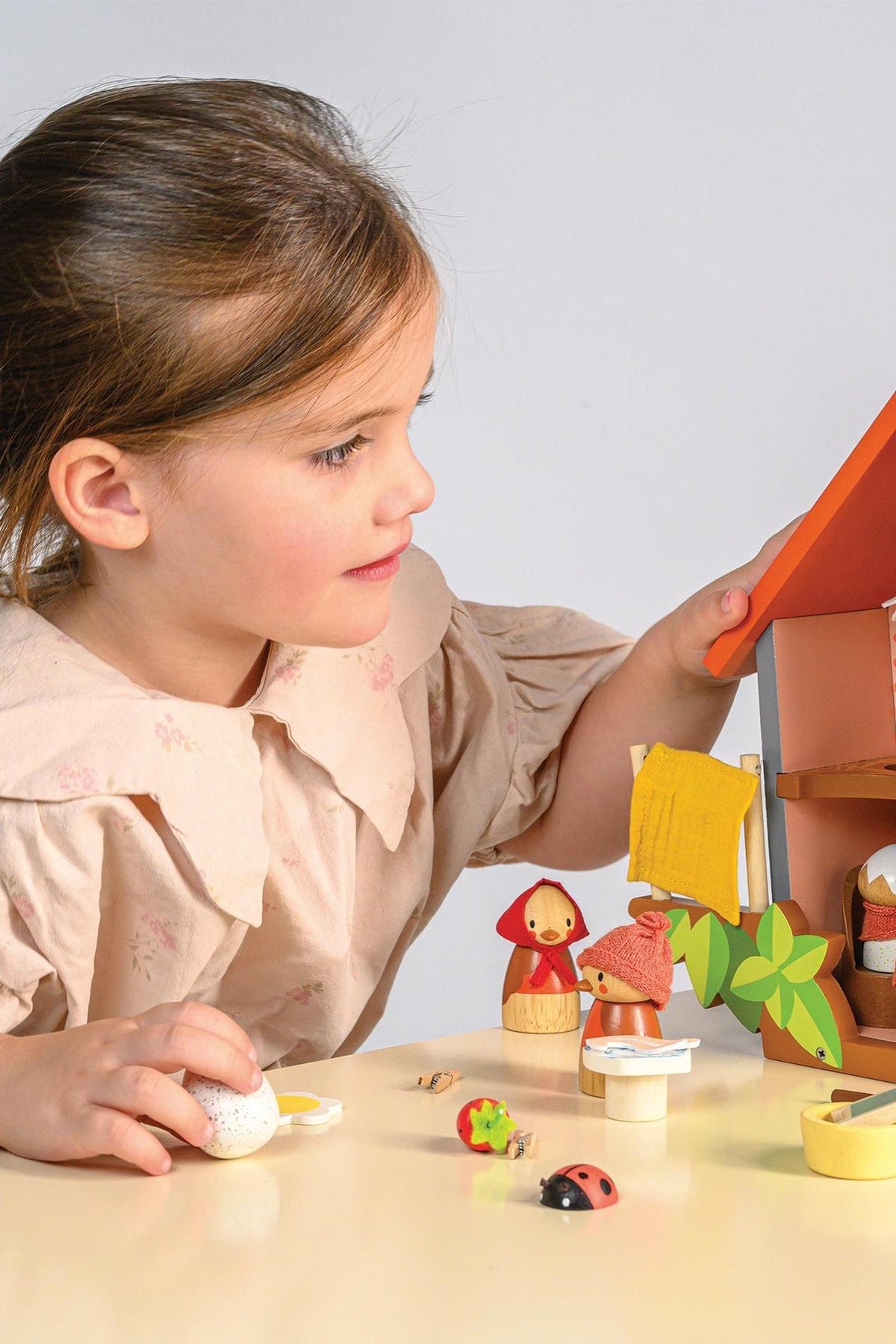 A child plays with Tender Leaf Wooden Toys, featuring colorful wooden bird figures and a house on a table.