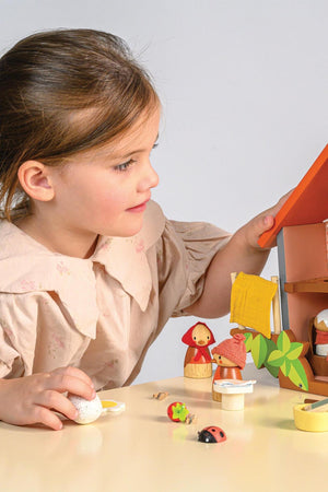 A child plays with Tender Leaf Wooden Toys, featuring colorful wooden bird figures and a house on a table.