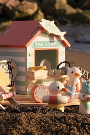 A colorful wooden beach hut labeled Sandys Fish & Chips with cheerful seagull figures, set on a sandy background.