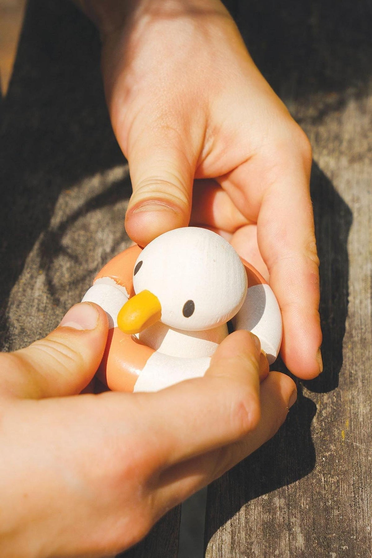 A child’s hands gently hold a wooden duck toy with an orange beak, accompanied by a life preserver.