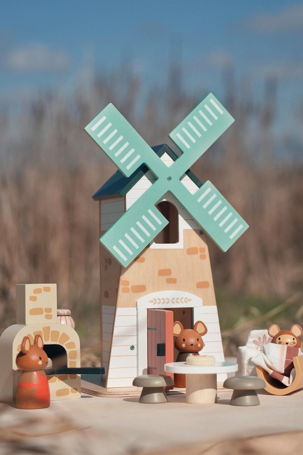 A colorful wooden playset features a two-story windmill with green blades, accompanied by three adorable field mice figures. This charming toy encourages imaginative play and is made from sustainable materials.