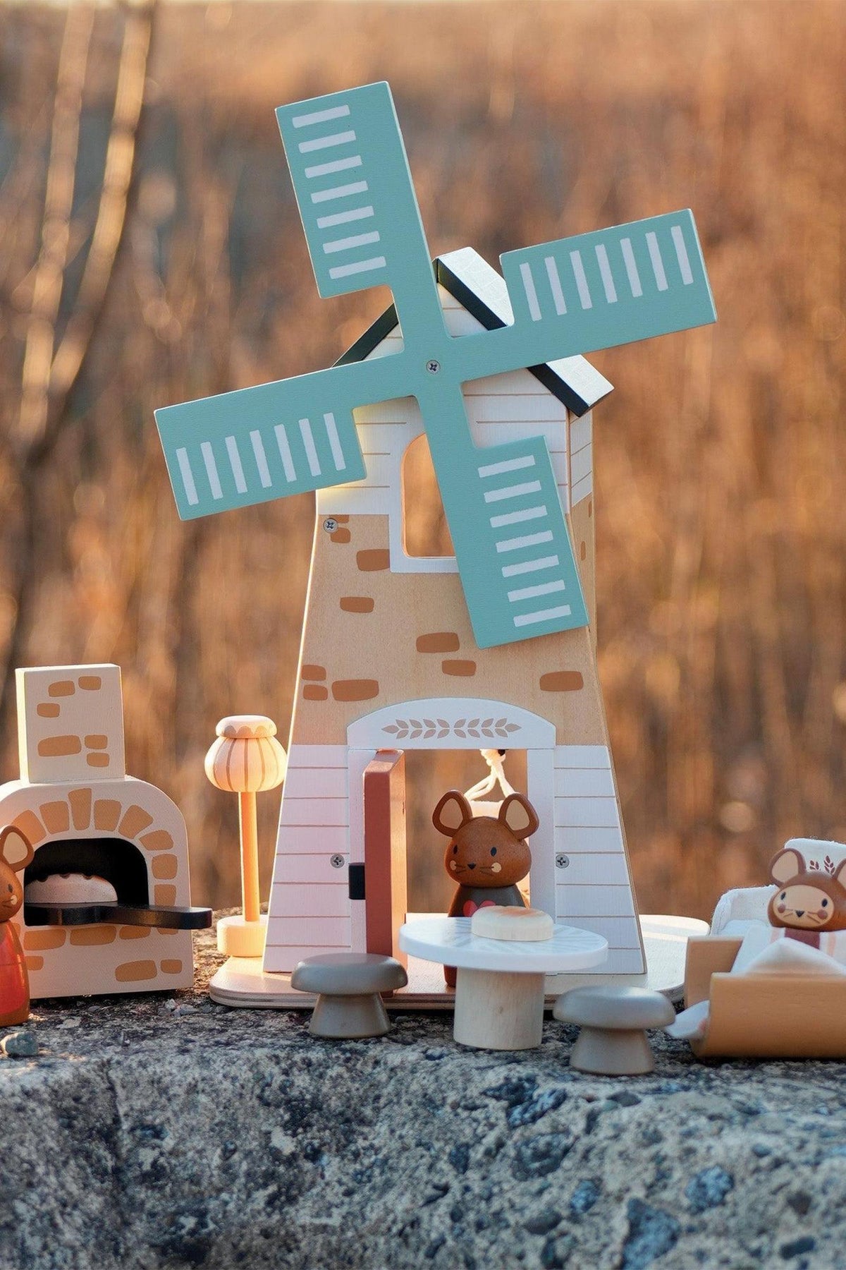 A charming wooden playset features a windmill with teal blades, accompanied by three adorable field mice and rustic accessories, set against a blurred natural background. Ideal for imaginative play.