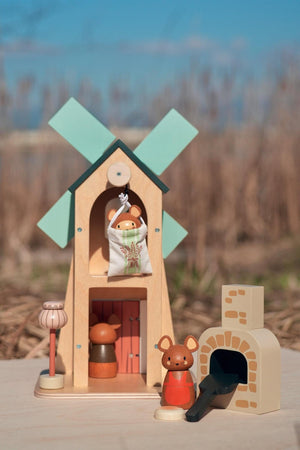 A whimsical wooden playset features a two-story structure with a green windmill, three small mice figures, and a charming brick oven, set against a natural outdoor backdrop.