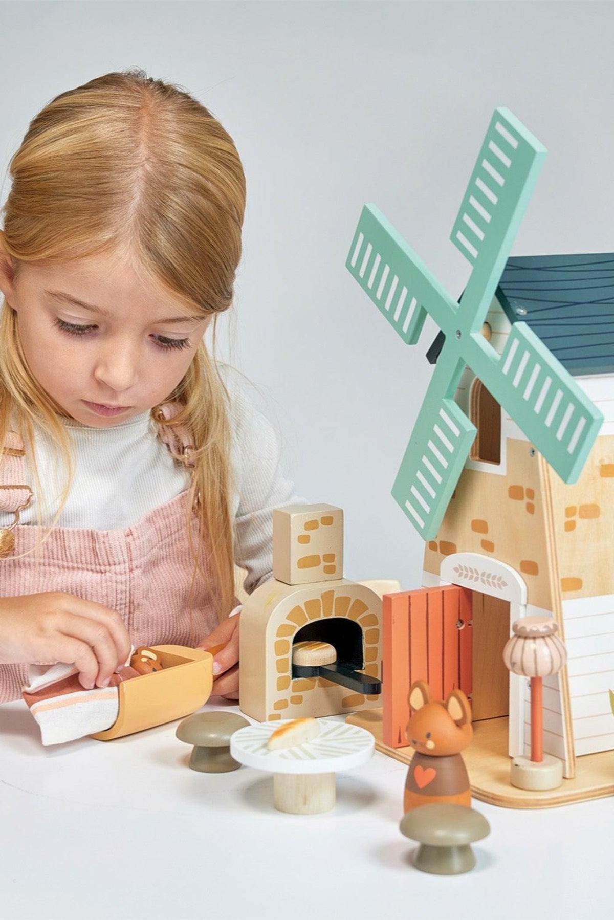 A young girl plays with the Tender Leaf Wooden Toys Penny Windmill set, featuring a colorful wooden windmill, cozy house, and charming animal figures, promoting imaginative and eco-friendly play.